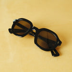 Front facing product image of Lesca Lunetier X Tombolo lenses in charcoal coloring with rounded square shaped lenses, folded up, on a yellow background