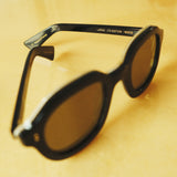 Lesca Lunetier X Tombolo side-facing product image in charcoal with emphasis on the individual engraving of each number of pair out 210 on the left branch while on a yellow background. 