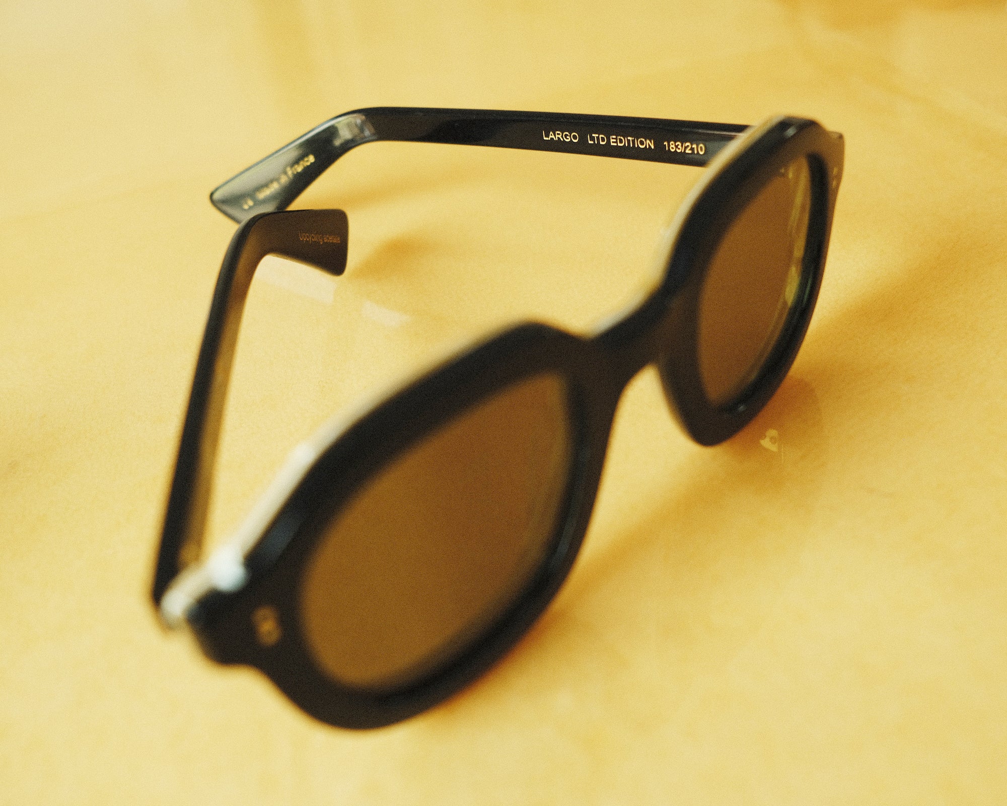 Lesca Lunetier X Tombolo side-facing product image in charcoal with emphasis on the individual engraving of each number of pair out 210 on the left branch while on a yellow background. 