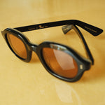 Lesca Lunetier X Tombolo lenses in Coral sideways-facing product image with emphasis on "Lesca x Tombolo" Logo graphics and 'upclycling acetate' denoting the types of material used to color the frame on a yellow background.