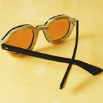 Lesca Lunetier X Tombolo lenses in Coral using a backward facing product image emphasising the inner layer of horn-colored acetate on the frame on a yellow background.