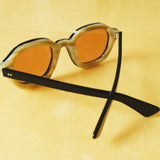 Lesca Lunetier X Tombolo lenses in Coral using a backward facing product image emphasising the inner layer of horn-colored acetate on the frame on a yellow background.