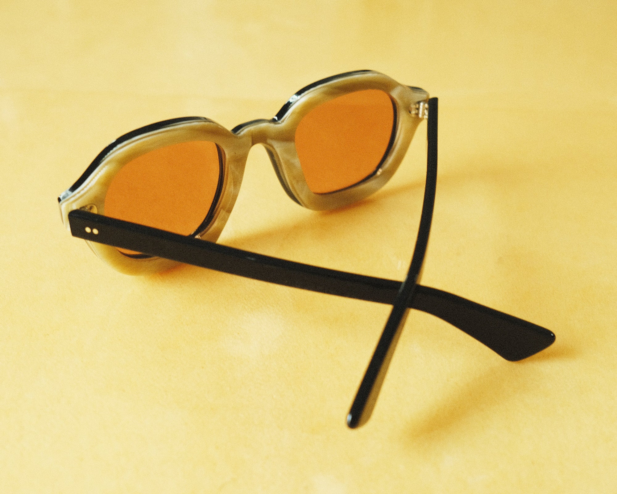 Lesca Lunetier X Tombolo lenses in Coral using a backward facing product image emphasising the inner layer of horn-colored acetate on the frame on a yellow background.