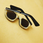 Lesca Lunetier X Tombolo lenses backwards-facing product image in charcoal coloring emphasizing the inner layer of horn-colored acetate with rounded square lenses on a yellow background.