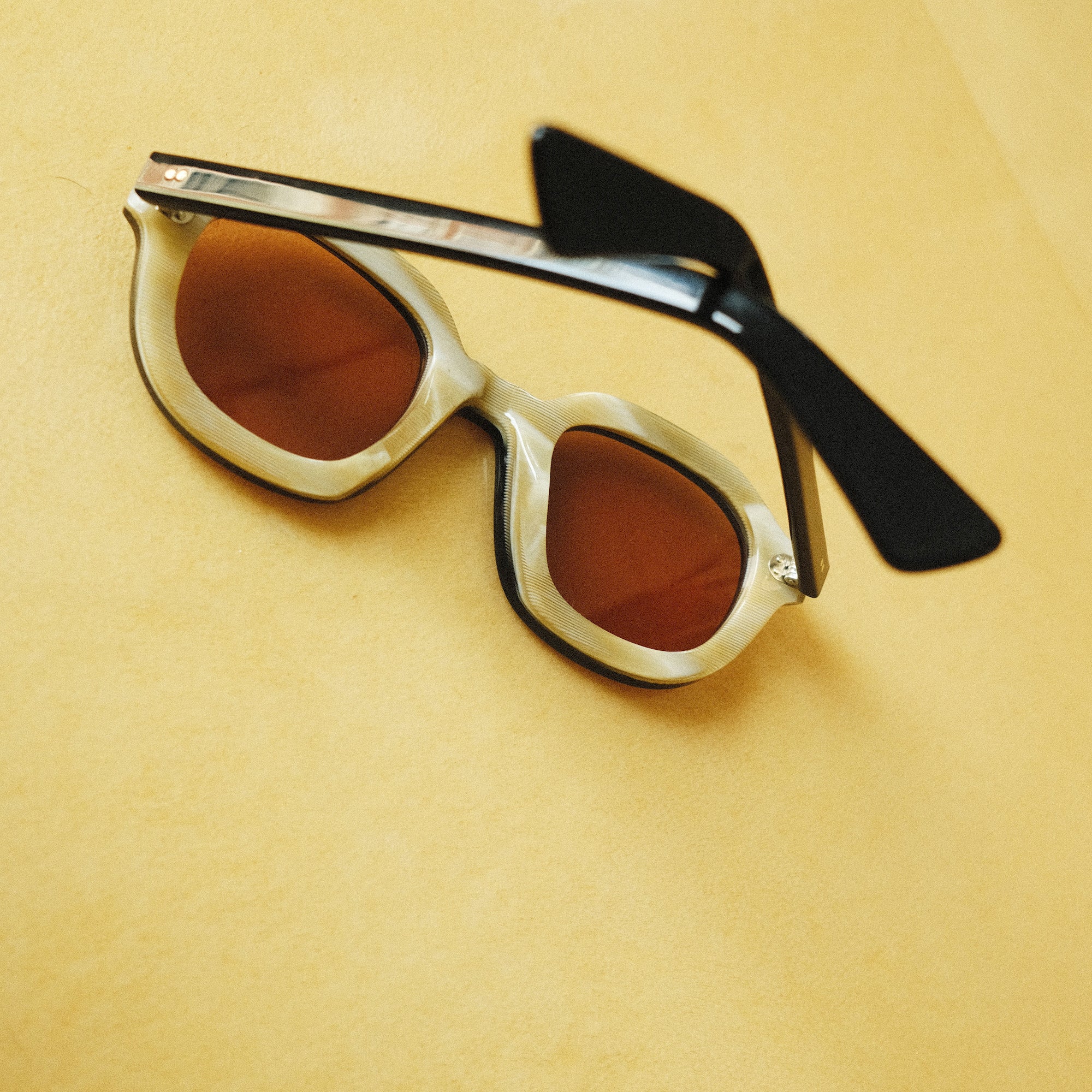 Lesca Lunetier X Tombolo lenses with a backwards-facing product image that emphasizes the inner layer of horn-colored acetate on a yellow background.
