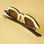 Lesca Lunetier X Tombolo lenses in charcoal using a backward facing product image emphasising the inner layer of horn-colored acetate on the frame on a yellow background.