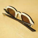 Lesca Lunetier X Tombolo lenses in charcoal using a backward facing product image emphasising the inner layer of horn-colored acetate on the frame on a yellow background.