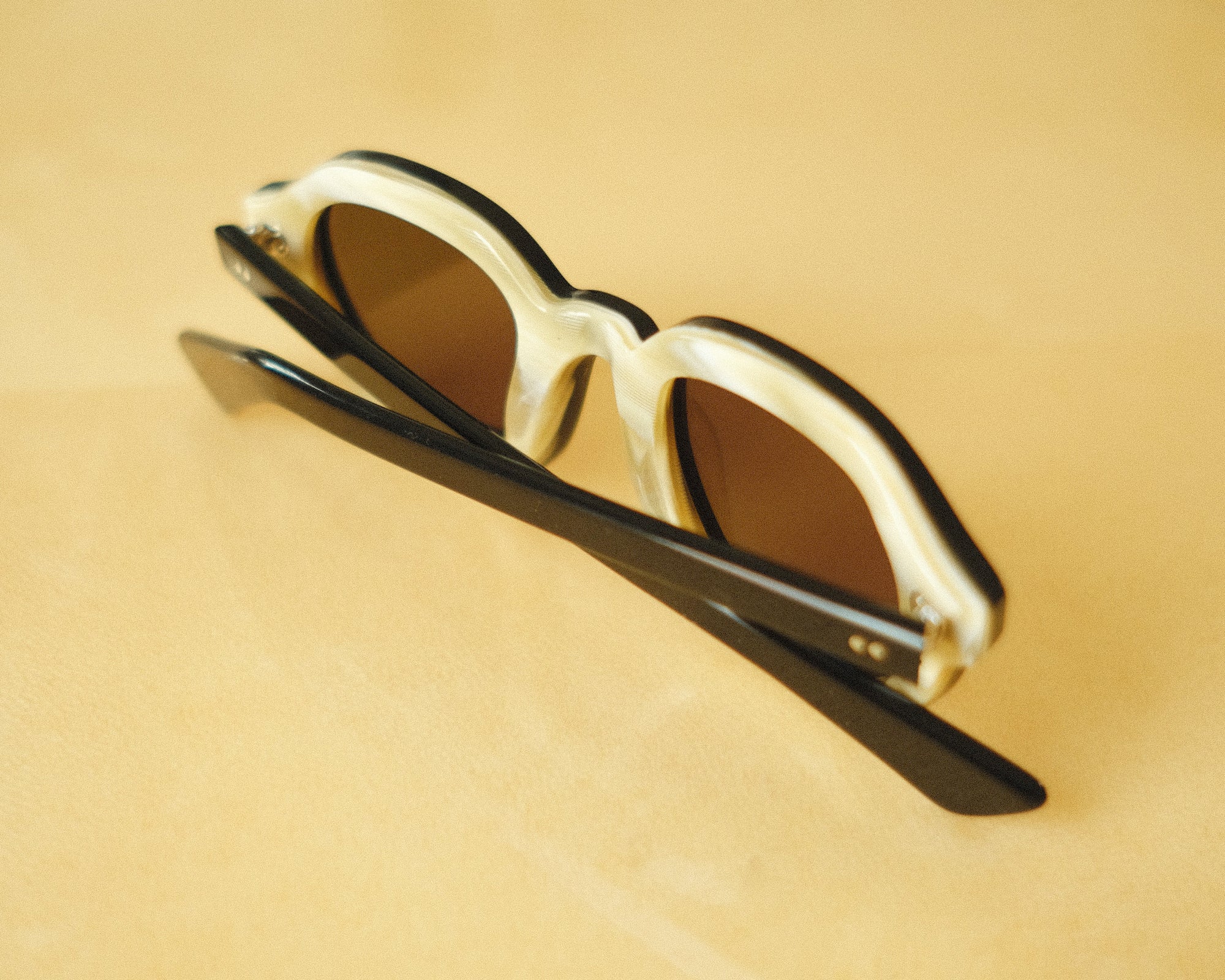 Lesca Lunetier X Tombolo lenses in charcoal using a backward facing product image emphasising the inner layer of horn-colored acetate on the frame on a yellow background.