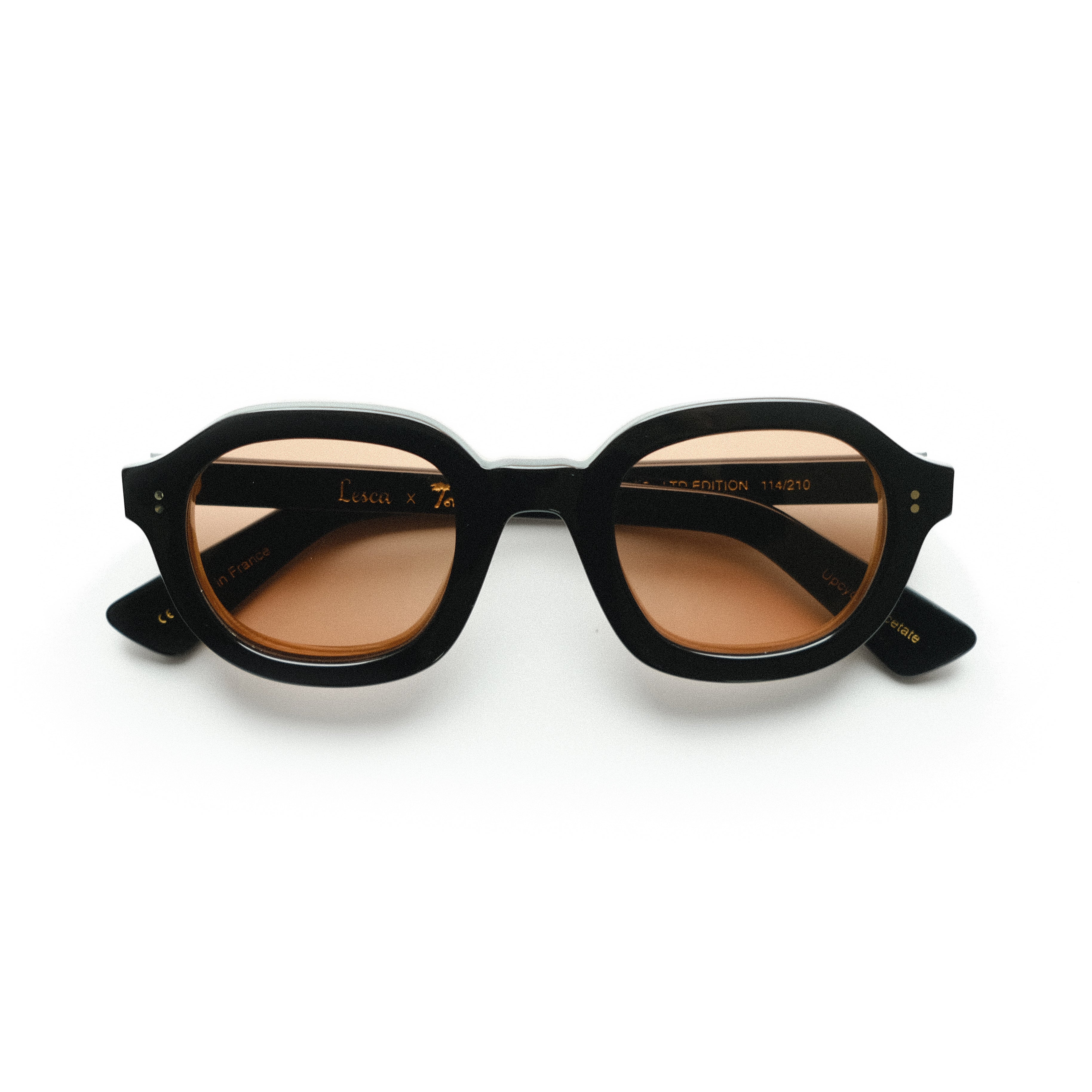 Lesca Lunetier x Tombolo Lenses front-facing product image with black frames and thick rounded lenses in a coral color on a white background.