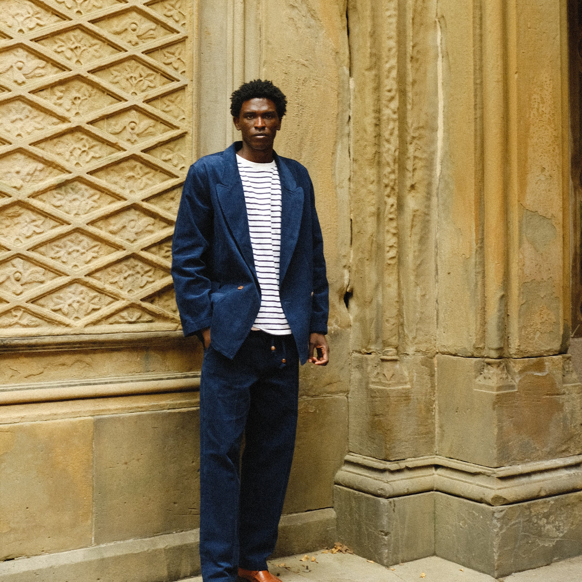 Man, standing outside, wearing the full Navy Corduroy Easy Going Set paired with brown shoes and a striped shirt. 