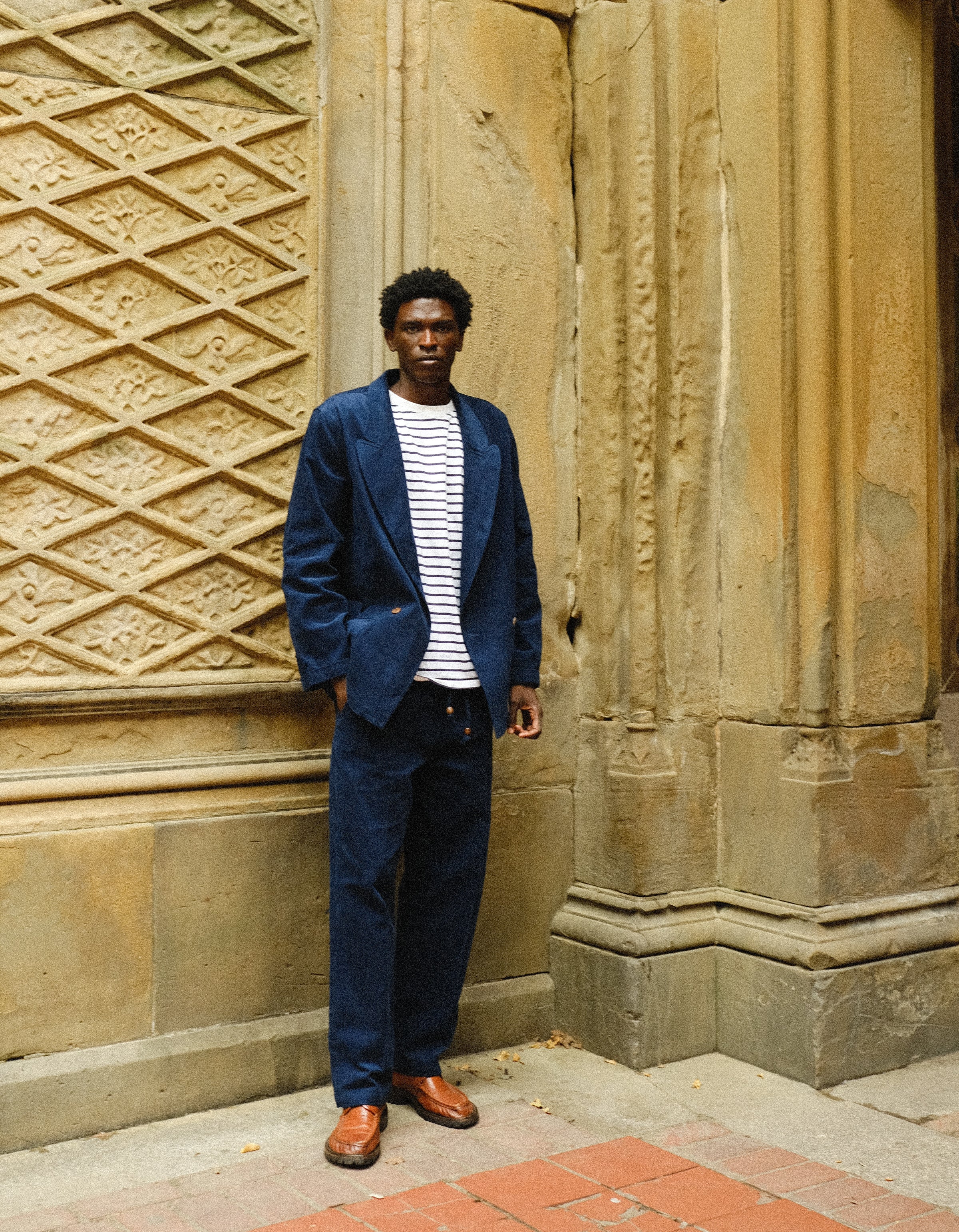 Man, standing outside, wearing the full Navy Corduroy Easy Going Set paired with brown shoes and a striped shirt. 