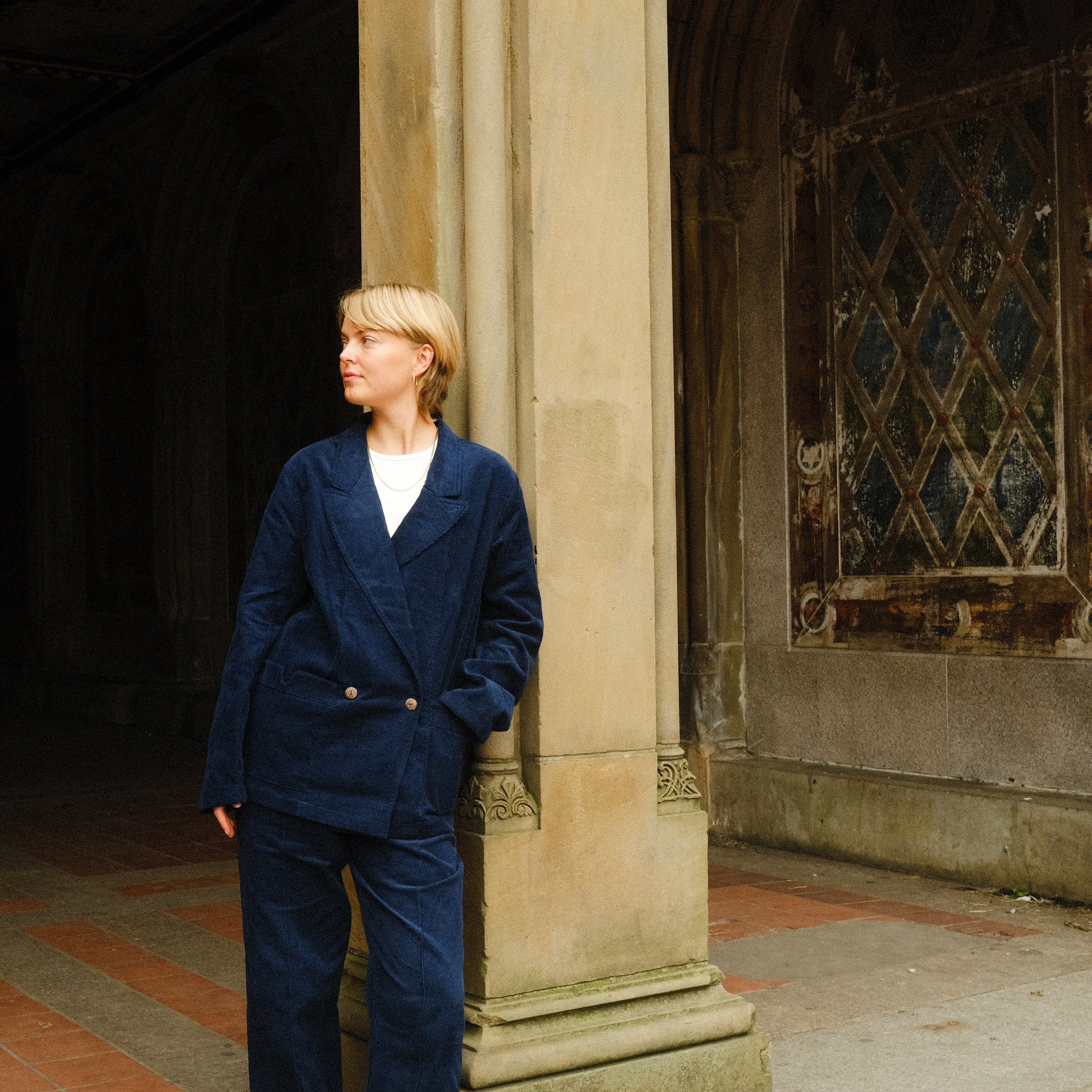 Woman, leaning against a pillar, wearing the full Navy Corduroy Easy Going Suit, with black loafers. 