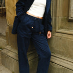 Close-up of a person wearing navy blue corduroy drawstring pants and a matching jacket, paired with a white cropped tank, white socks, black loafers, and a gold chain necklace.