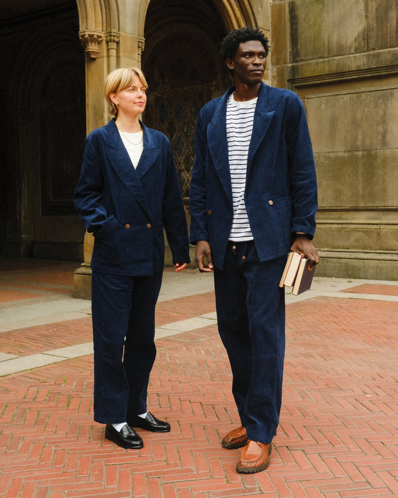 A man and woman are seen, both wearing the full Navy Corduroy Easy Going Suits. The man is carrying a few books, and the two of them are looking off camera. 