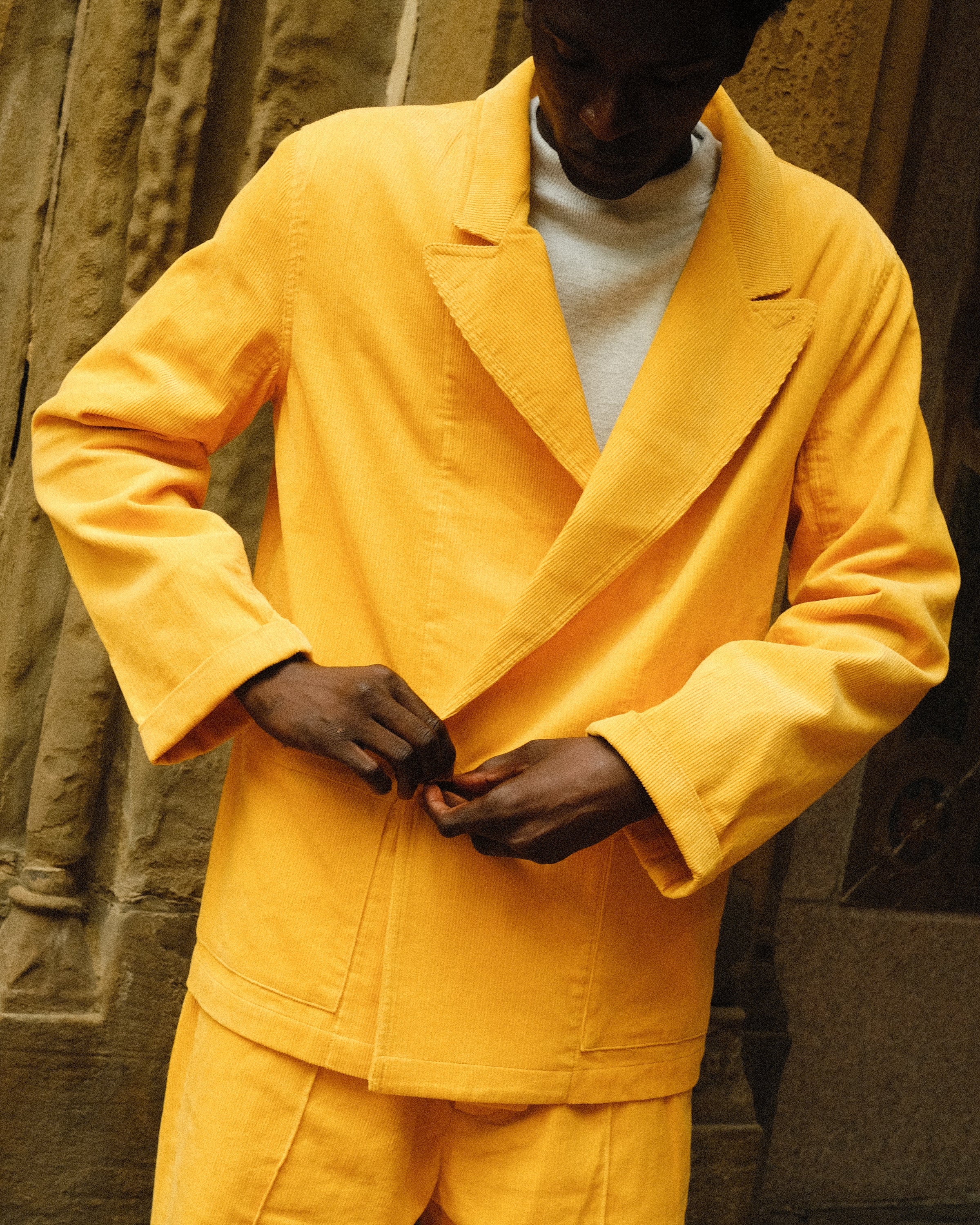 Man wearing full yellow corduroy 'Easy Going Suit'. He is looking down and buttoning up the jacket. 