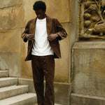 Man wearing a brown corduroy jacket and matching pants, paired with a plain white T-shirt and brown loafers.