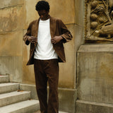 Man wearing a brown corduroy jacket and matching pants, paired with a plain white T-shirt and brown loafers.