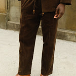 Close-up of a person wearing brown corduroy drawstring pants with a matching jacket, paired with a white shirt and brown loafers.