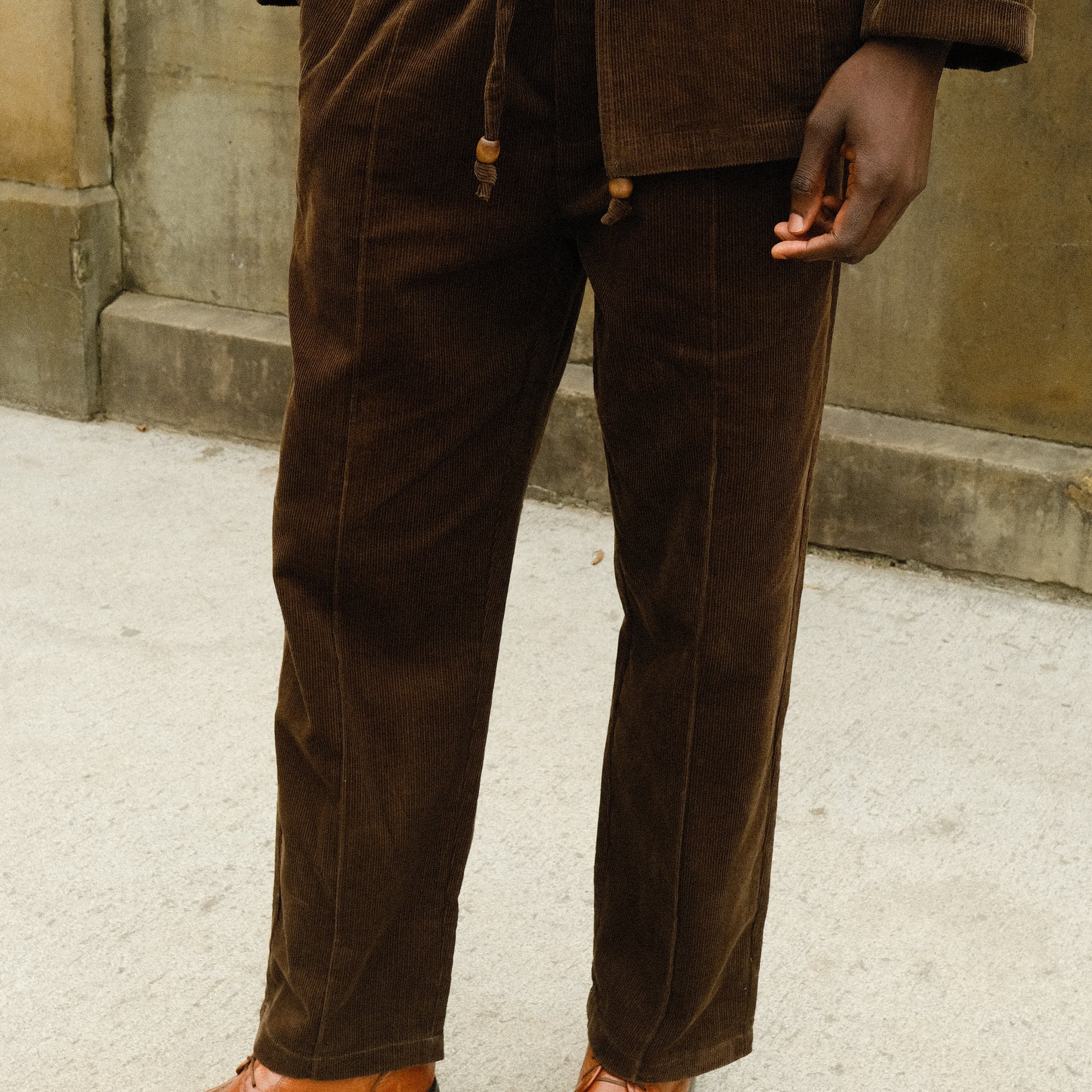 Close-up of a person wearing brown corduroy drawstring pants with a matching jacket, paired with a white shirt and brown loafers.