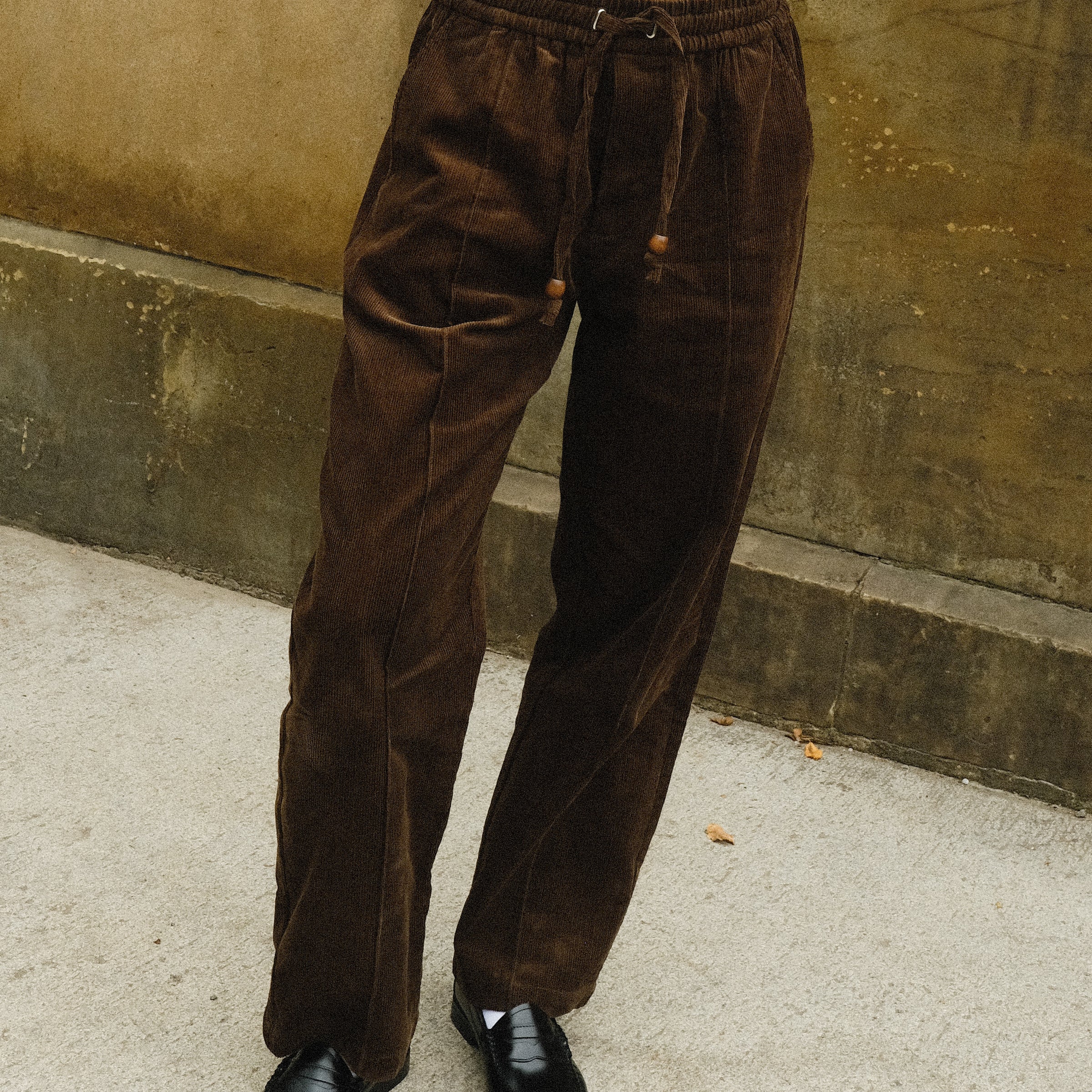 Close-up of a person wearing brown corduroy drawstring pants with a white sleeveless top and black loafers.