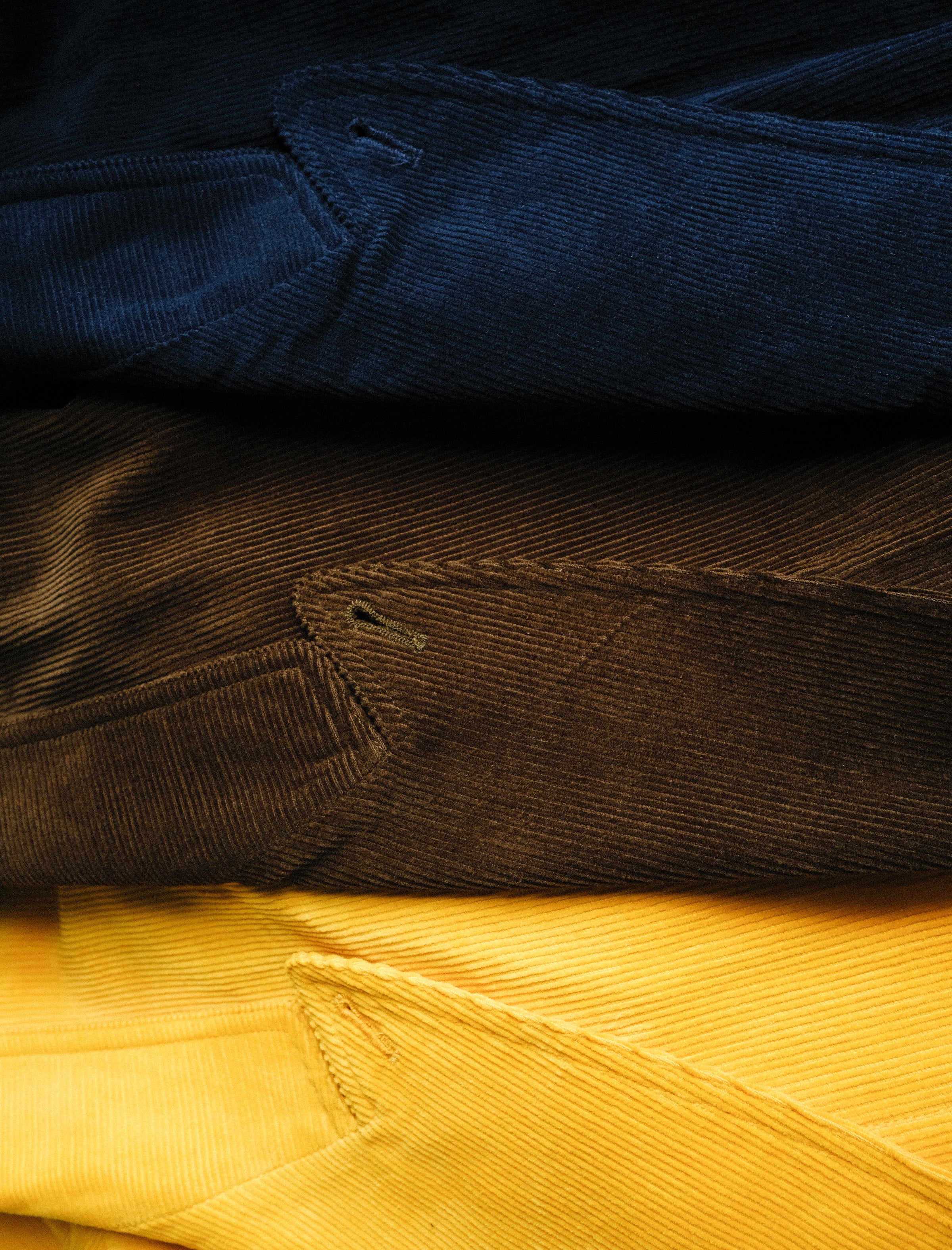Saffron, brown, and navy corduroy jackets are seen folded on top of each other. 