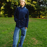 Woman wearing a navy blue corduroy jacket buttoned to the top, paired with loose-fitting blue jeans and black shoes.
