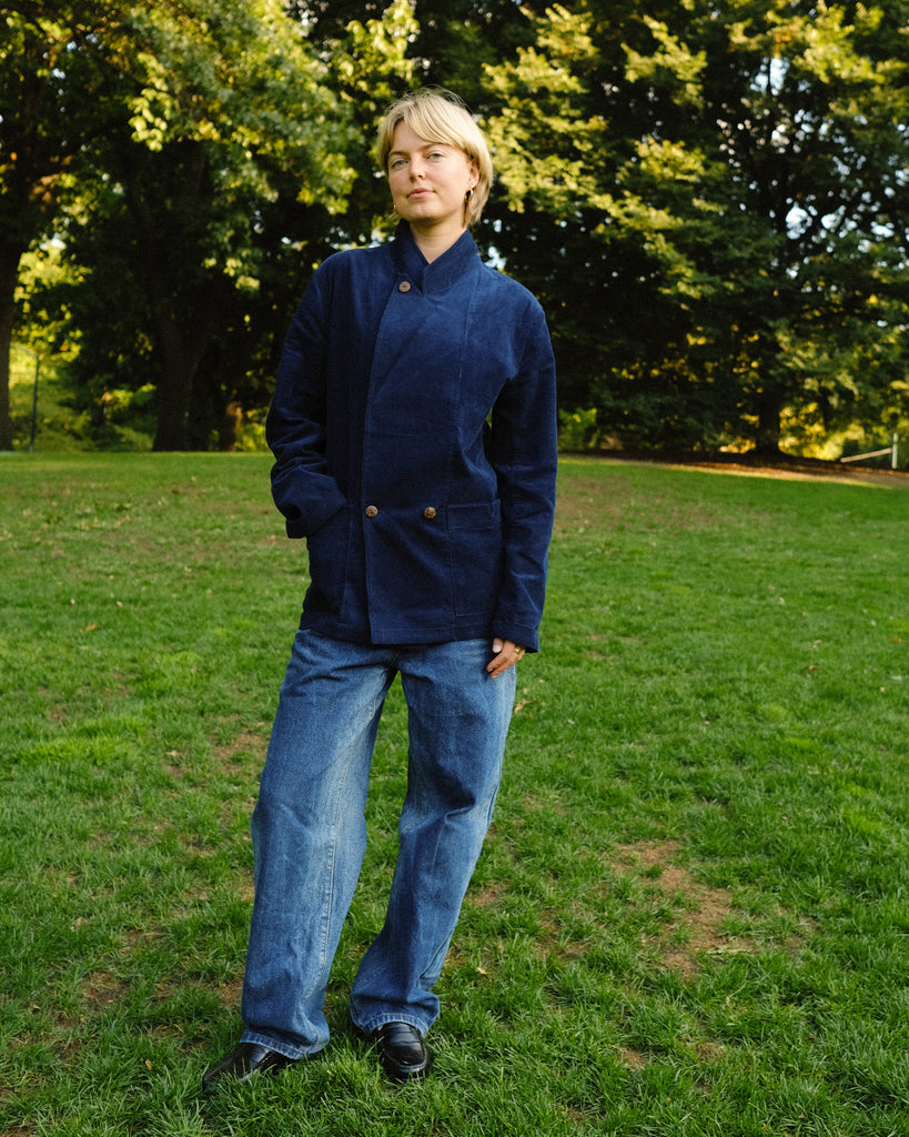 Woman wearing a navy blue corduroy jacket buttoned to the top, paired with loose-fitting blue jeans and black shoes.