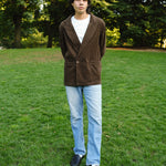  Man wearing a brown corduroy jacket over a white T-shirt, paired with light blue jeans and black loafers.
