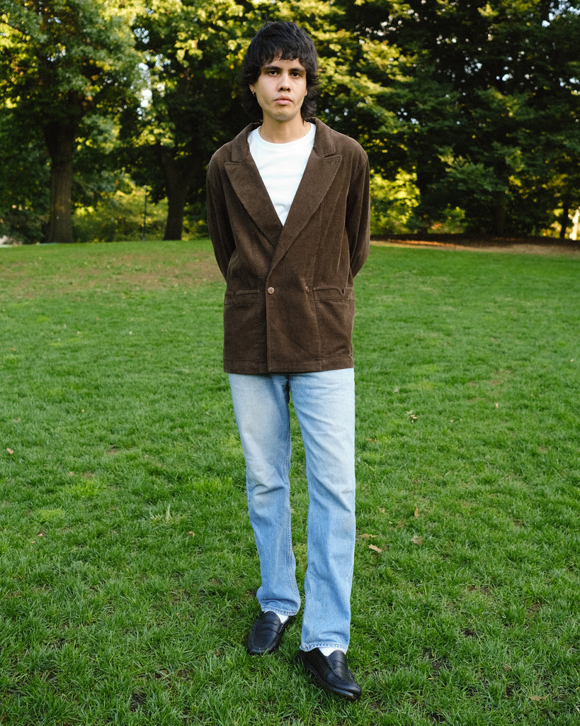  Man wearing a brown corduroy jacket over a white T-shirt, paired with light blue jeans and black loafers.