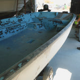 Rust-covered boat on a trailer with a person in an orange shirt and jeans standing nearby.