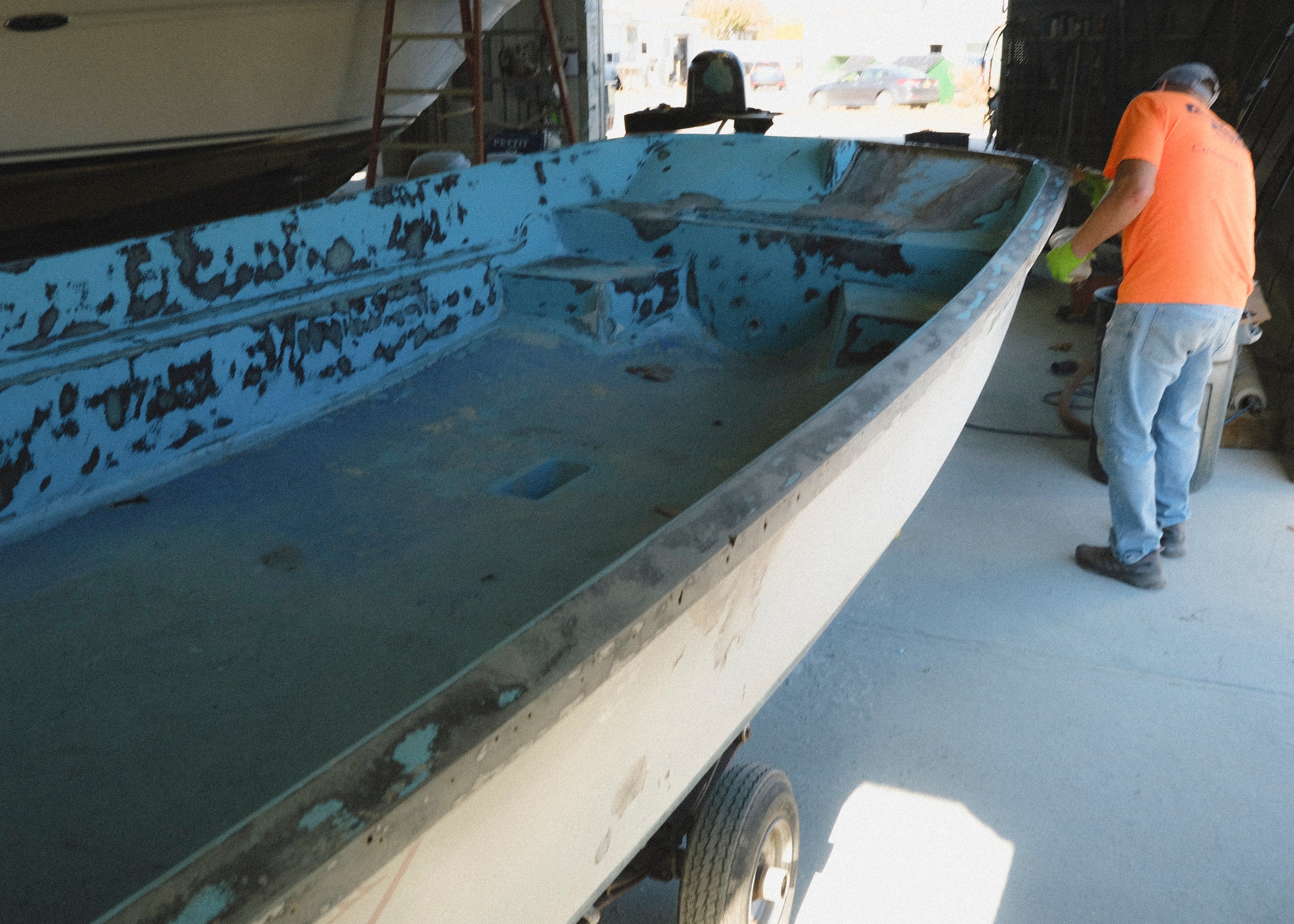 Rust-covered boat on a trailer with a person in an orange shirt and jeans standing nearby.