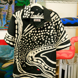 Black short sleeve cabana shirt with cream chain-stitch embroidery in a loon-inspired abstract pattern, hanging on a rack.