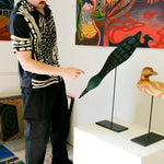 Model wearing black cabana shirt with cream loon-inspired chain-stitch embroidery, pointing at loon sculpture.