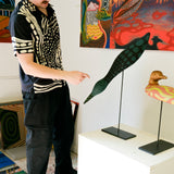 Model wearing black cabana shirt with cream loon-inspired chain-stitch embroidery, pointing at loon sculpture.