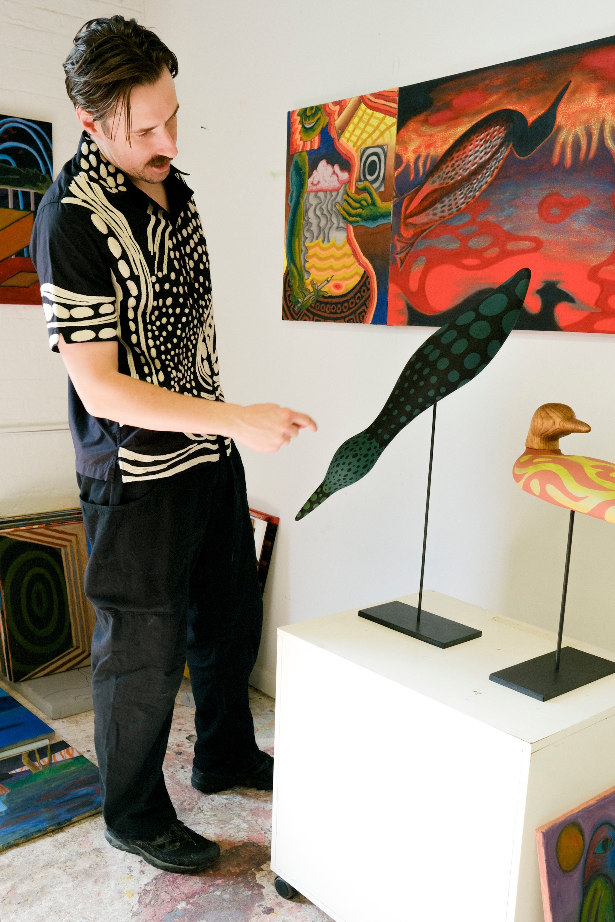 Model wearing black cabana shirt with cream loon-inspired chain-stitch embroidery, pointing at loon sculpture.