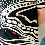 Close-up of black cabana shirt with cream chain-stitch embroidery in a loon-inspired dotted and wave pattern, with red stitched detail.