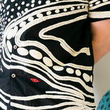 Close-up of black cabana shirt with cream chain-stitch embroidery in a loon-inspired dotted and wave pattern, with red stitched detail.