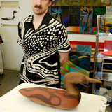 Artist, Julian MacMillan wearing black cabana shirt with cream loon-inspired chain-stitch embroidery, standing beside a carved loon sculpture.
