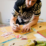 Model wearing black cabana shirt with cream loon-inspired chain-stitch embroidery while writing on labels.