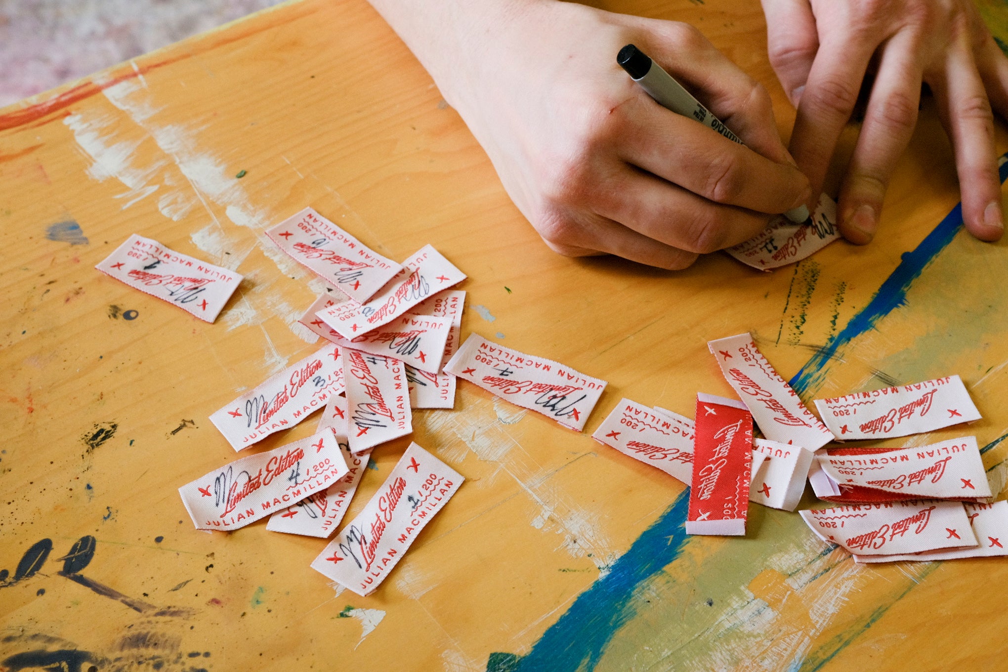 Close-up of hands signing limited edition labels for Julian MacMillan collaboration.