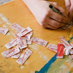 Close-up of hands signing limited edition labels for Julian MacMillan collaboration.