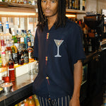 Male mode is pictured wearing the 'Extra Dirty' ~ Relaxed Fit while standing behind the bar of a restaurant. He paired the shirt with a pair of our Easy-Going Jacquard Stripe Pants. 