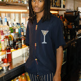 Male mode is pictured wearing the 'Extra Dirty' ~ Relaxed Fit while standing behind the bar of a restaurant. He paired the shirt with a pair of our Easy-Going Jacquard Stripe Pants. 