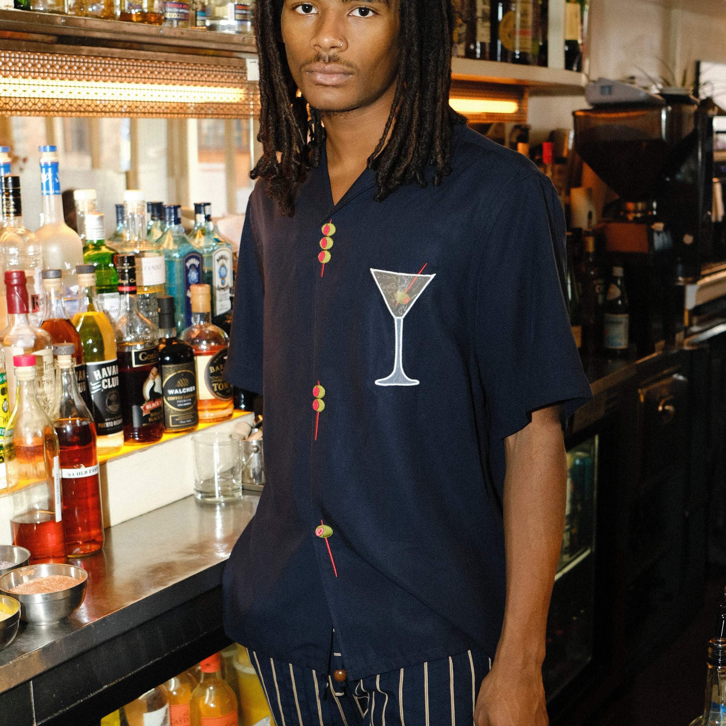 Male mode is pictured wearing the 'Extra Dirty' ~ Relaxed Fit while standing behind the bar of a restaurant. He paired the shirt with a pair of our Easy-Going Jacquard Stripe Pants. 