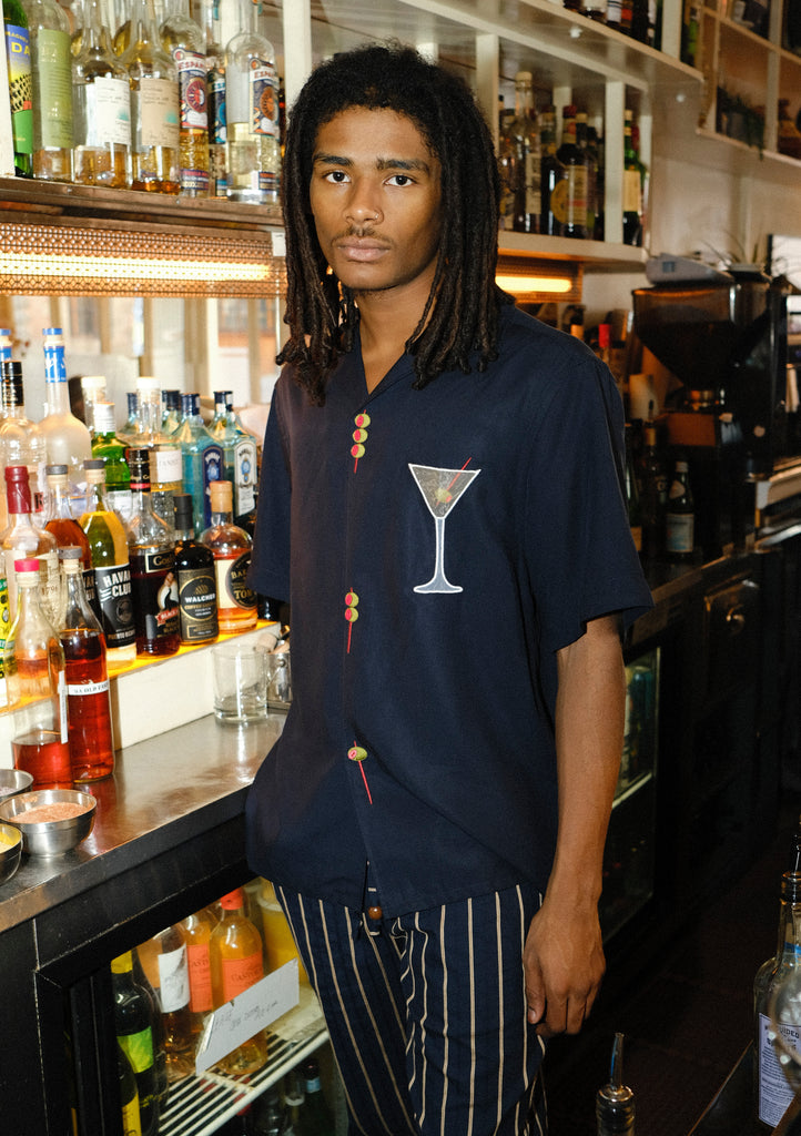 Male mode is pictured wearing the 'Extra Dirty' ~ Relaxed Fit while standing behind the bar of a restaurant. He paired the shirt with a pair of our Easy-Going Jacquard Stripe Pants. 