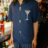 Cropped image of male model in restaurant bar, standing next to alcohol, wearing the 'Extra Dirty' ~ Relaxed Fit and our Easy Going Pants in Navy Jacquard Stripe. 