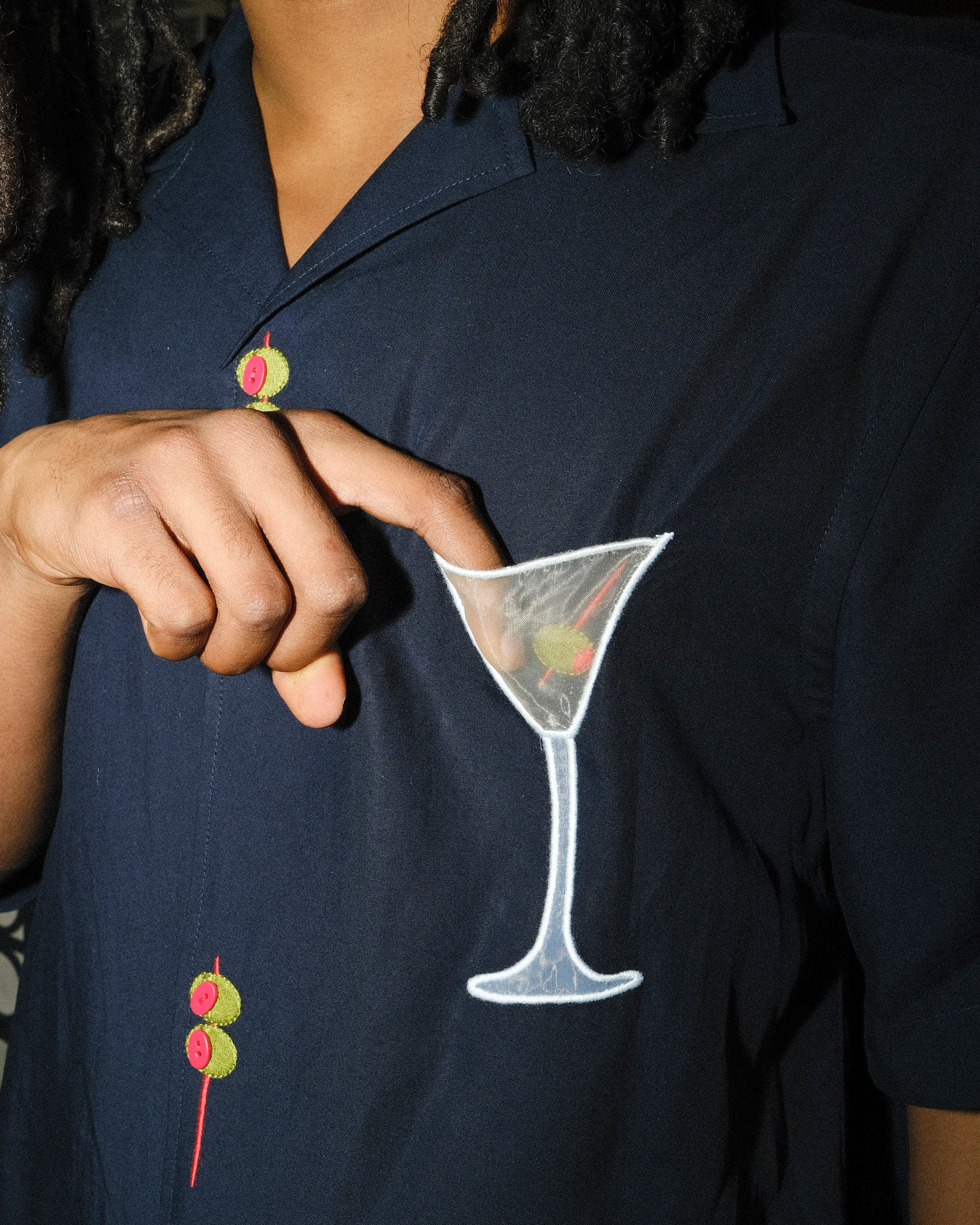 A detailed look at the mesh martini pocket appliqué on the 'Extra Dirty' shirt. The model’s fingertip subtly reveals the sheer quality of the mesh