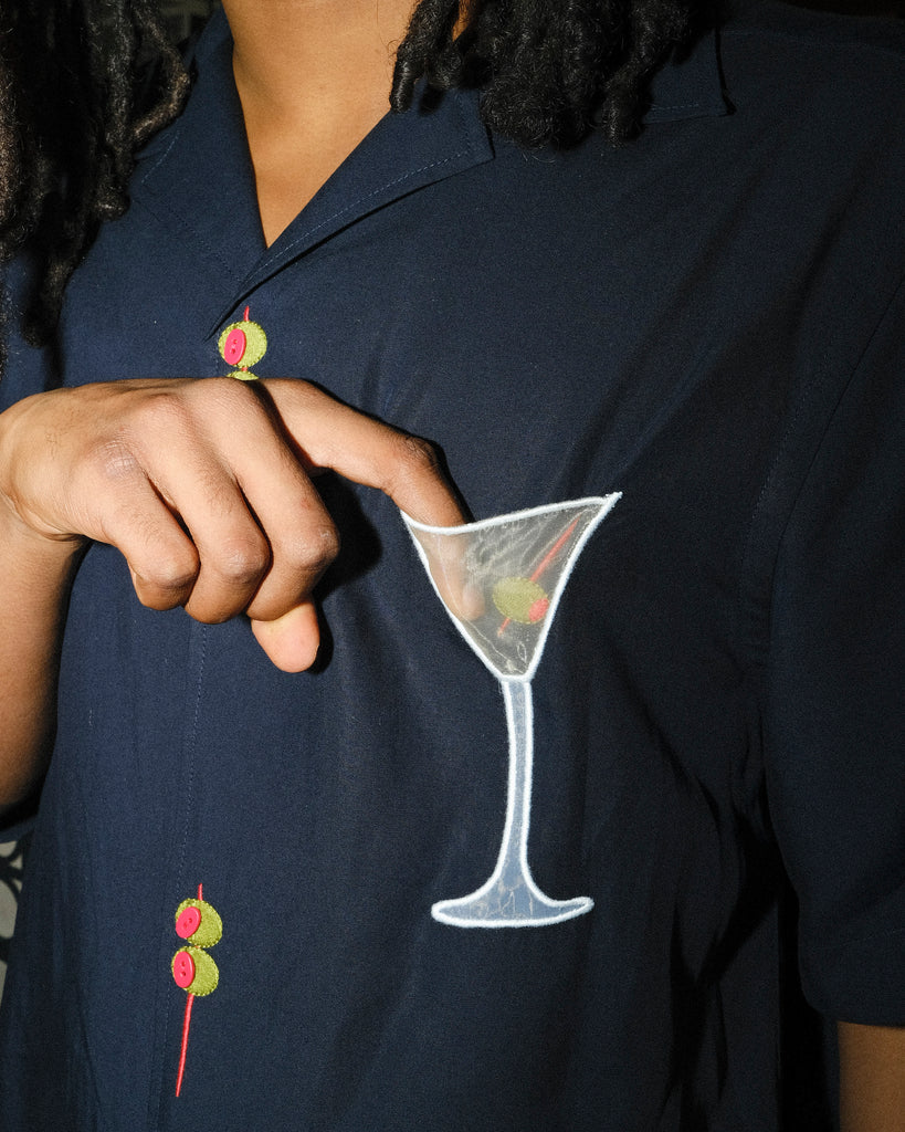 A detailed look at the mesh martini pocket appliqué on the 'Extra Dirty' shirt. The model’s fingertip subtly reveals the sheer quality of the mesh