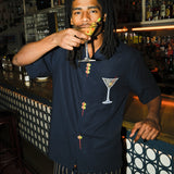 Image of model standing at the bar, sipping on a dirty martini, wearing the 'Extra Dirty' ~ Relaxed Fit Shirt and our Striped Easy Going Pants. 