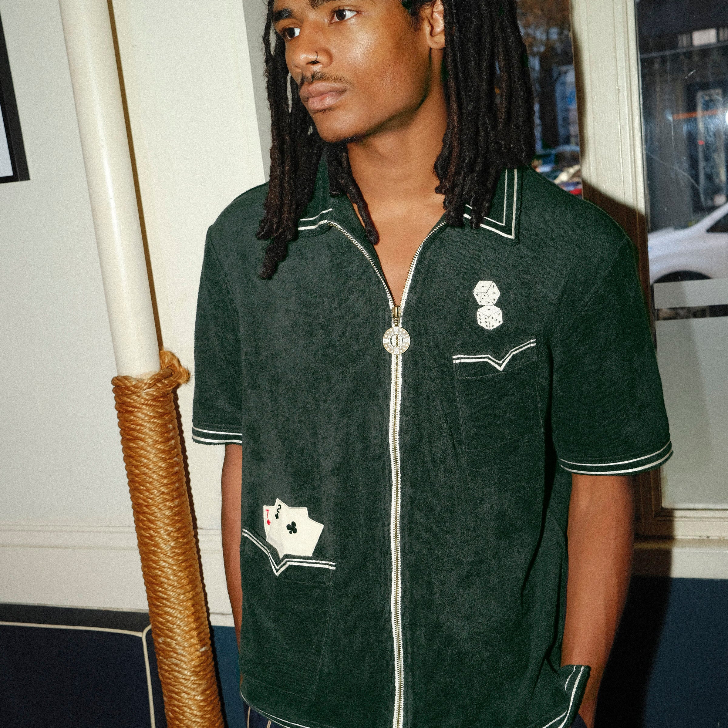 Model looking left, wearing a green terrycloth shirt with playing card and dice embroidery by Tombolo